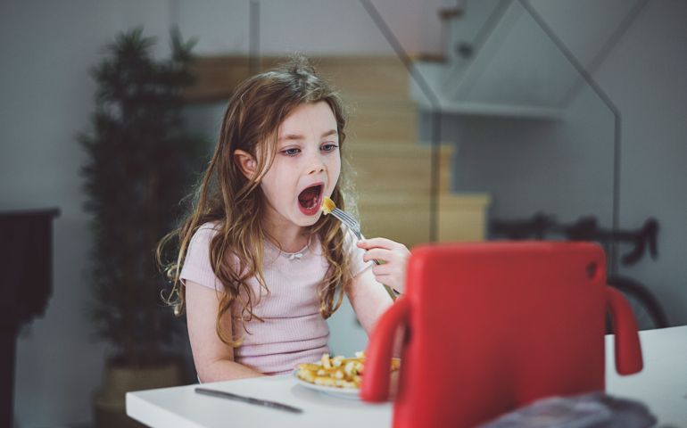 Young girl eating dinner watching tablet