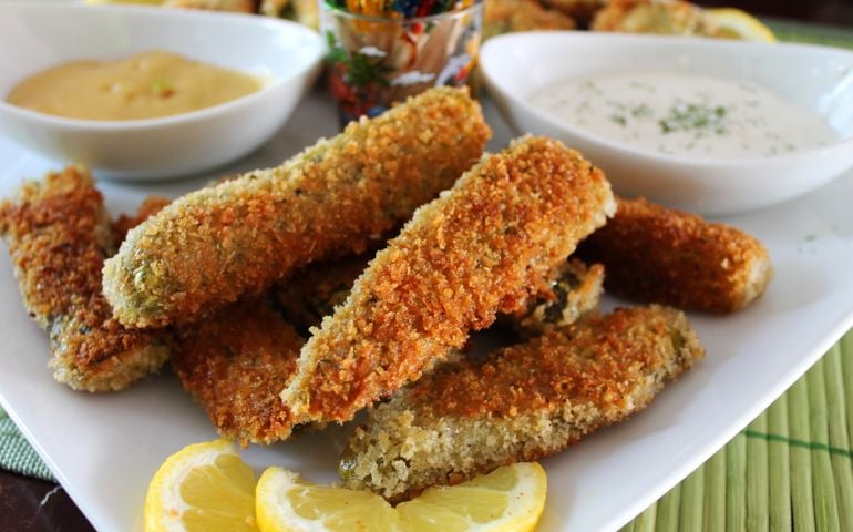 Deep fried dill pickles, with dipping sauce, and sour cream and chives. White plate and bowls, colorful toothpicks.