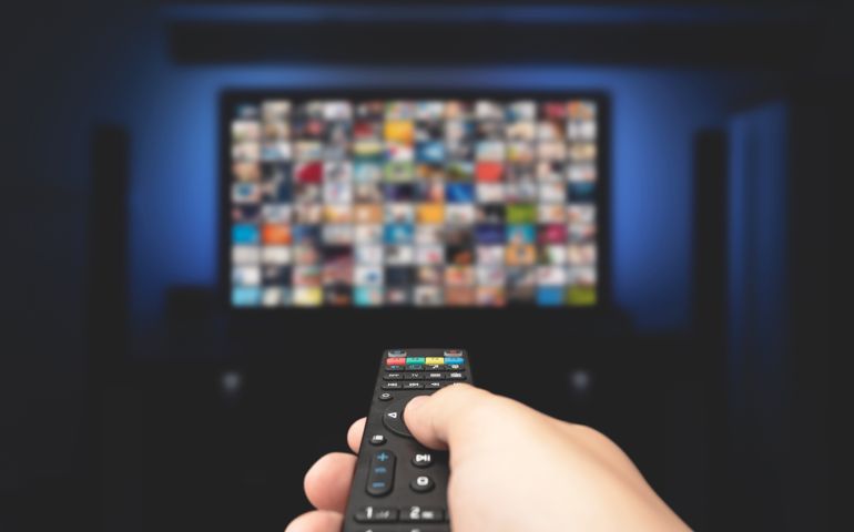 Multimedia video concept on TV set in dark room. Man watching TV with remote control in hand.