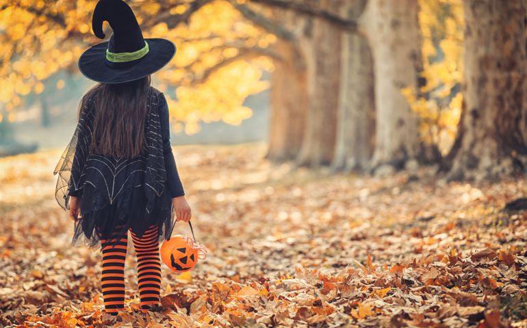 Little girl in witch costume having fun outdoors on Halloween trick or treat