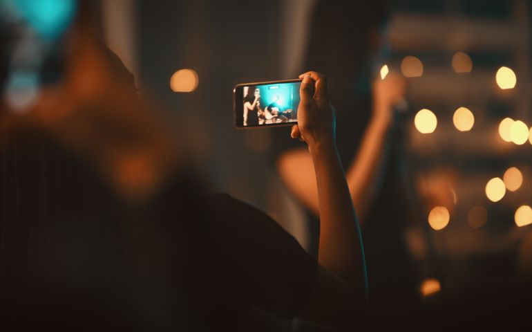 Closeup shot of an unrecognisable woman in the audience capturing a performance at the club on a cellphone