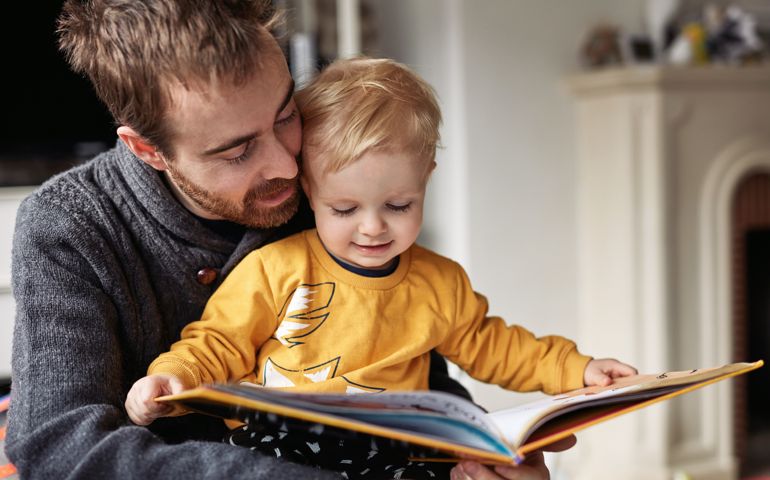 Cropped shot of an adorable little boy reading a book while sitting with his father at home