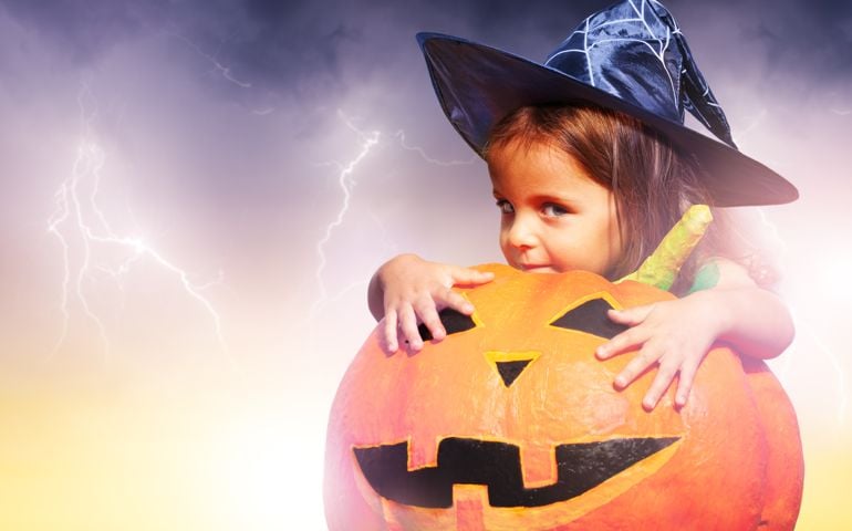 Little girl in Halloween costume sit with orange scary big pumpkin