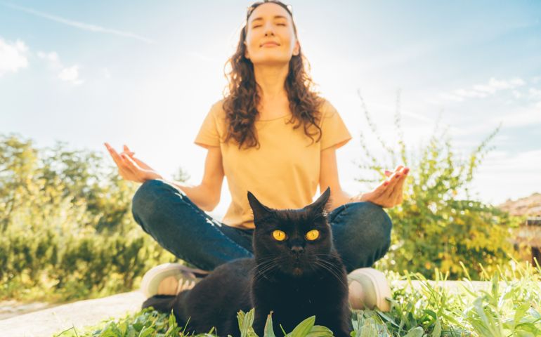 Picture of young woman meditating in the garden sitting with her black cat