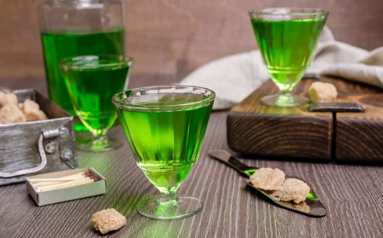 Green liquid in a glass with sugar cubes on a dark wooden background. Selective focus.