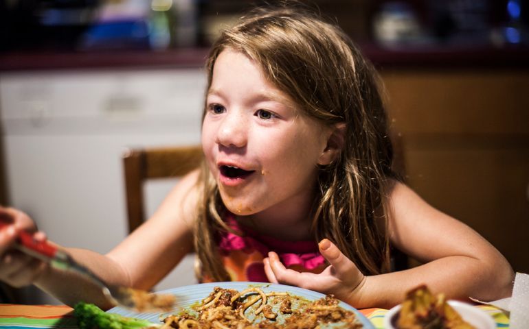 girl (5 yrs) talking with family at dinner table
