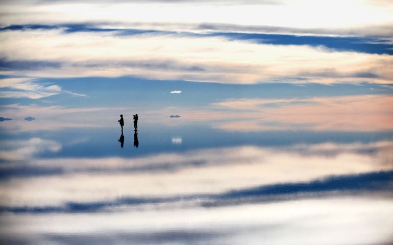 Two tourist stand in shallow water at the Salar de Uyuni, Bolivia