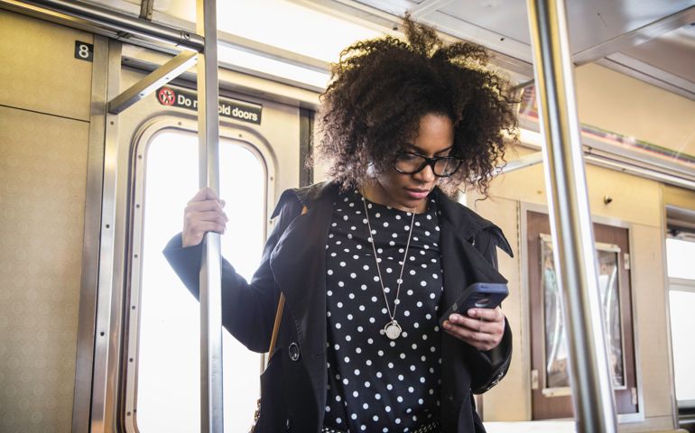 A young woman commuting on the subway and using her phone to catch up on emails