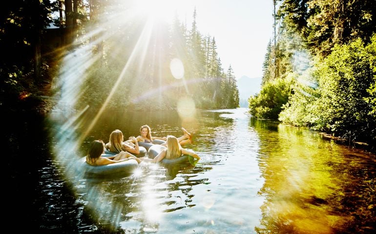 Laughing group of female friends floating on river in inner tubes on summer afternoon
