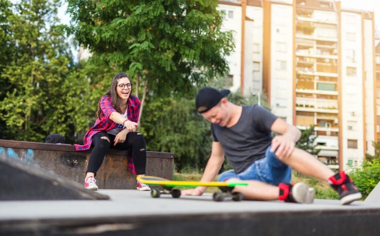 19 years old couple. They love to spend their free time together at the skateboard park. She is laughing because she told him that he will fall down, and he didn't listen to her