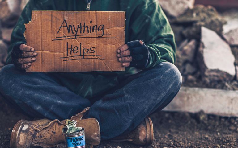 Fighting adversity. Homeless man with sign and money tin