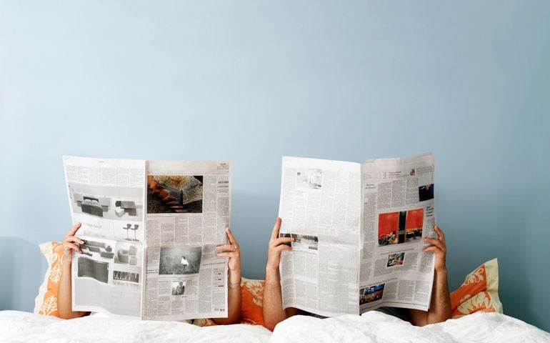 Young couple reading newspaper on bed