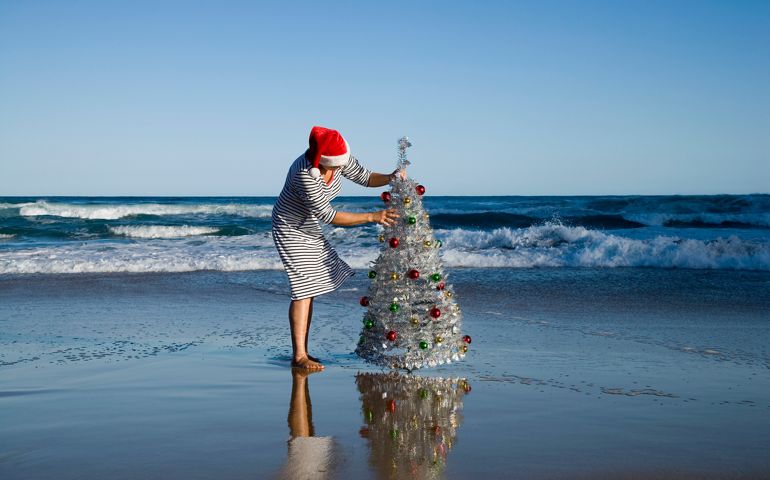 Woman decorating Christmas tree on beach, side vie