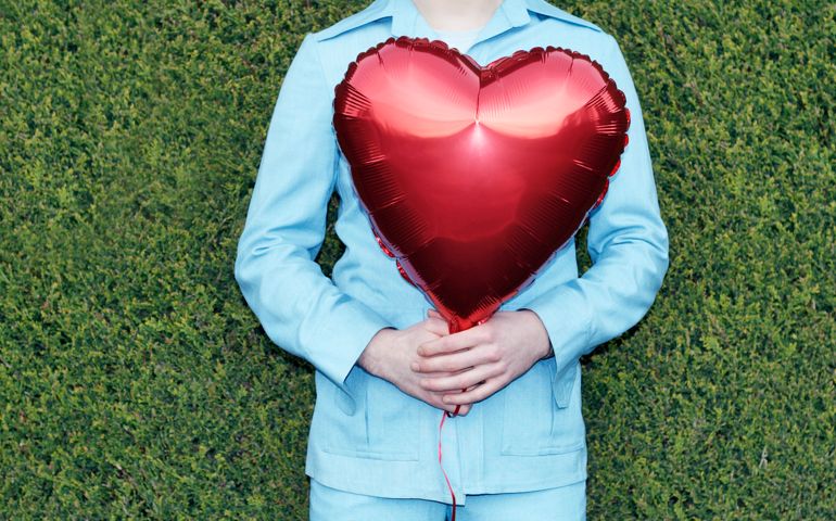 Young man in safari suit holding red heart shaped balloon, mid section