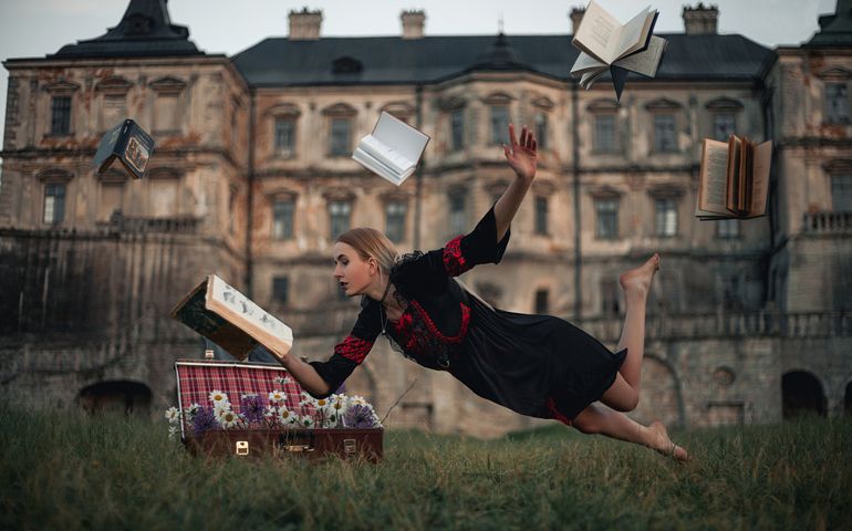 Woman sorceress reads book and flies in air against backdrop of ancient castle.