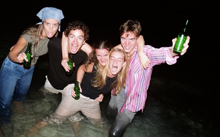 Group of young people in sea holding bottles of beer, portrait