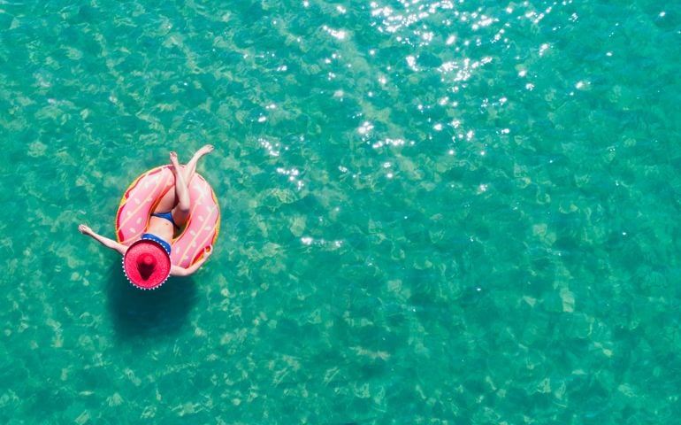 Lady floating in the sea in a rubber ring, wearing large hat