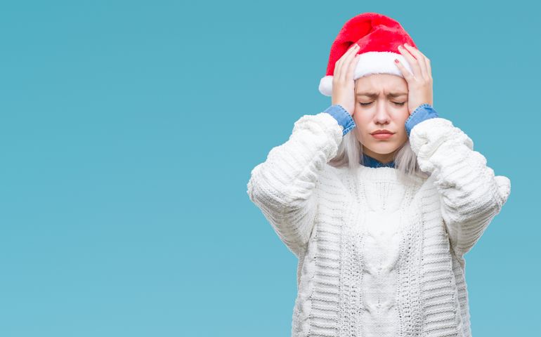 Young blonde woman wearing christmas hat over isolated background suffering from headache desperate and stressed because pain and migraine. Hands on head.