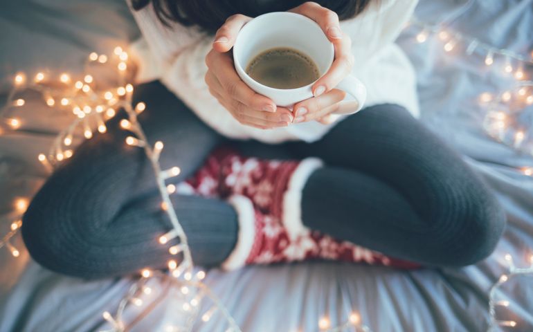 Woman sitting at home legs crossed on bed, holding a cup of coffee, christmas decoration.