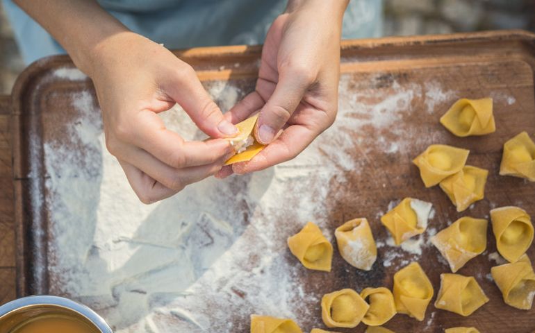 Young woman chef preparing handmade tortellini stuffed with ricotta and cheese. Tortellini, also known as cappelletti, are ring-shaped pasta, sometimes also described as "navel shaped", hence their alternative name of "belly button" (ombelico). They are typically stuffed with a mix of meat (pork loin, prosciutto) or cheese. Originally from the Italian region of Emilia (in particular Bologna and Modena), they are usually served in broth, either of beef, chicken, or both.
