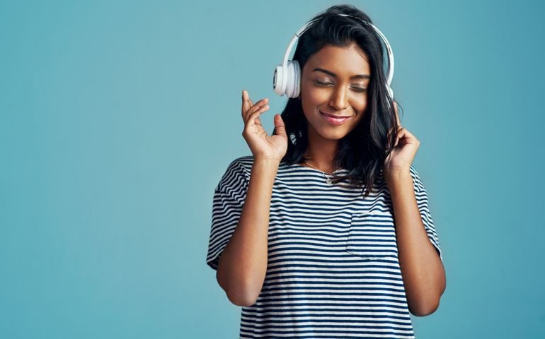 Cropped shot of a beautiful young woman wearing headphones against a blue background