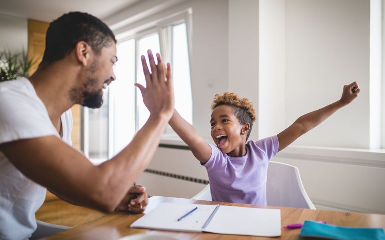 Cute and lovely mixed race girl doing homework at home, with a help of her father.