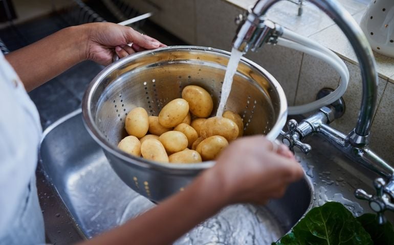 Cropped shot of a woman rinsing potatoes in a kitchen sink at home