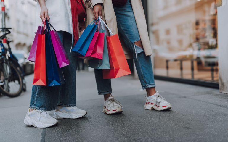 Look what we bought. Close up of two girl in jeans and sneakers holding colorful shopping bags