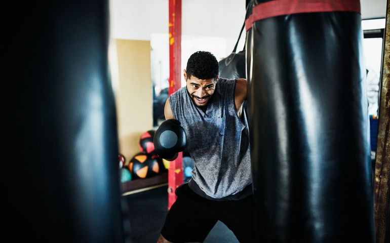 Male boxer punching heavy bag in gym