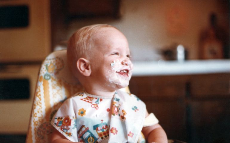 Smiling one year old baby boy with his face covered in cake and icing on his very first birthday.