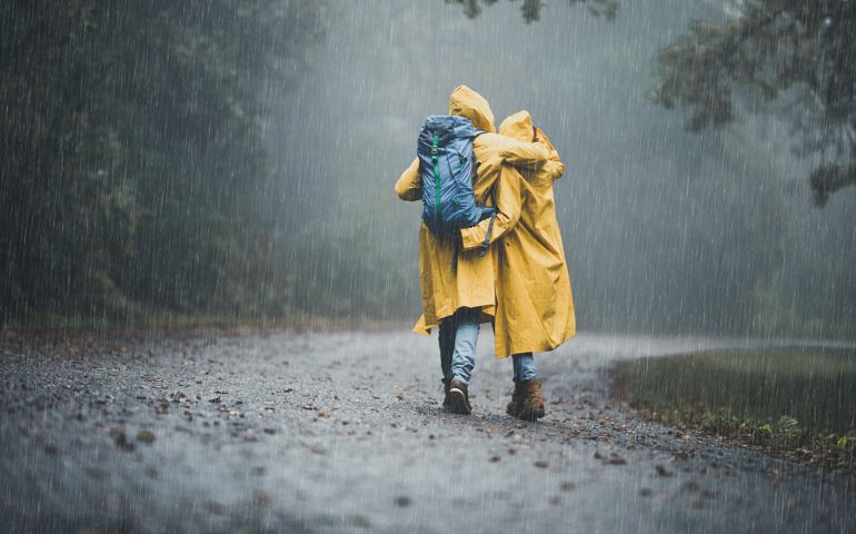 Rear view of loving couple in yellow raincoats hiking through park on a rainy day. Copy space.