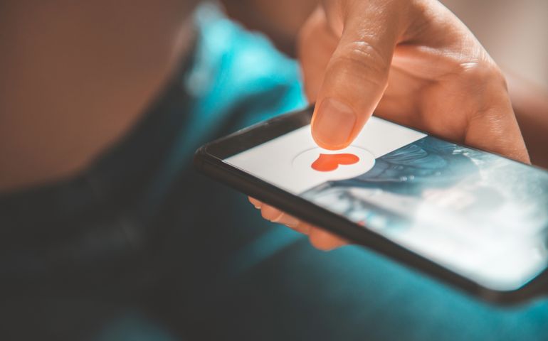 Finger of woman pushing heart icon on screen in mobile smartphone application. Online dating app, valentine's day concept.