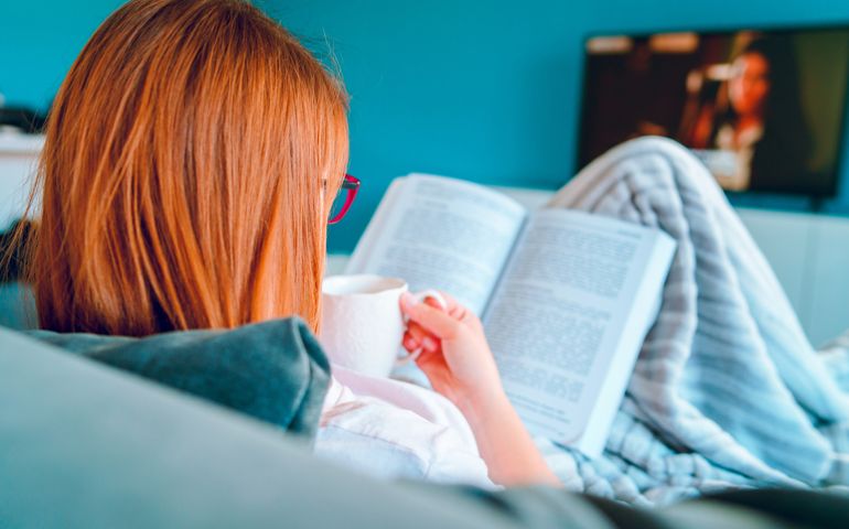 Young beautiful woman caucasian girl reading a book in bed wearing eyeglasses and having a cup of coffee at home student study