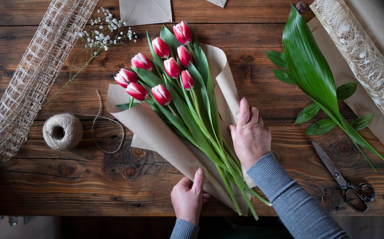 Top view of unrecognizable woman arrange Tulips on wooden table, woman's hands creating a bouquet of flowers.