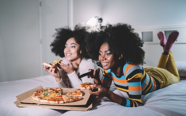 Girlfriends eating pizza in bed and watching TV