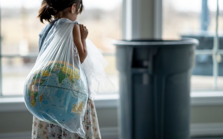 Little girl walking bagged globe over to garbage can because generations before her didn't take care of Mother Earth.