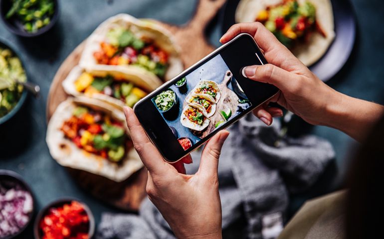 Hand of a chef taking photograph of tacos on table with a mobile phone. Hands of cook photographing Mexican food .