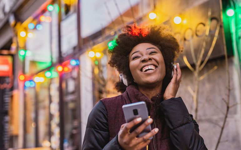 A young woman is using a mobile phone and wireless headphones outdoor during Christmas