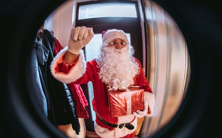 Santa Claus knocking in door and holding gift.