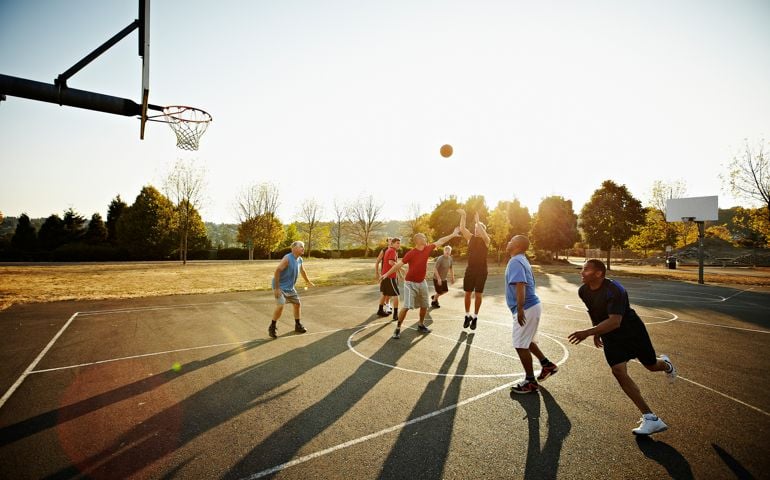 Group of senior and mature men playing basketball on outdoor court at sunset