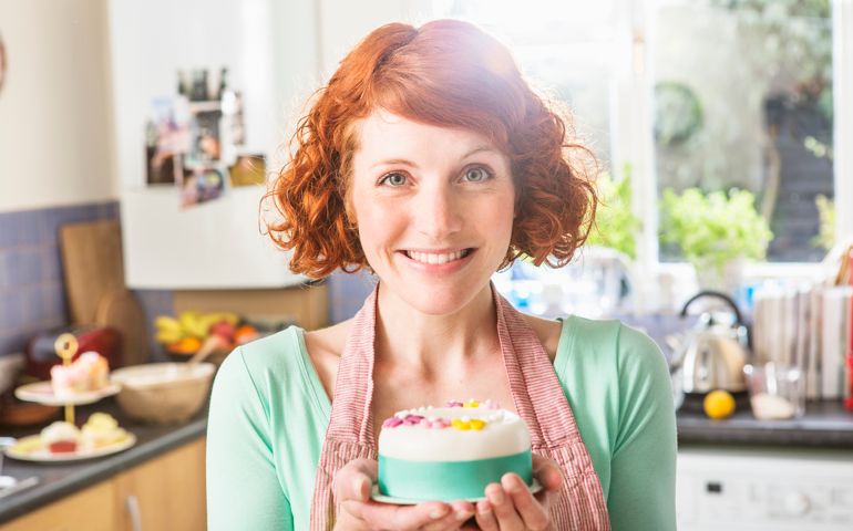 Woman holding decorated icing cake, in kitchen.