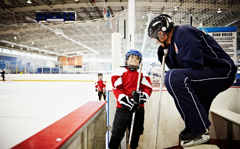 Ice hockey coach encouraging young ice hockey player in players box teammates out on ice