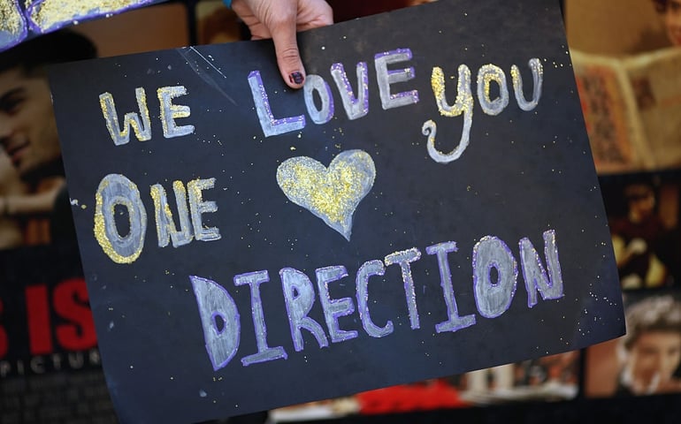 One Direction fans wave placards as they take their positions in Leicester Square ahead of the premier to the bands new film on August 20, 2013 in London, England. The bands new film, 'This Is Us', will premier this evening at the Empire cinema.