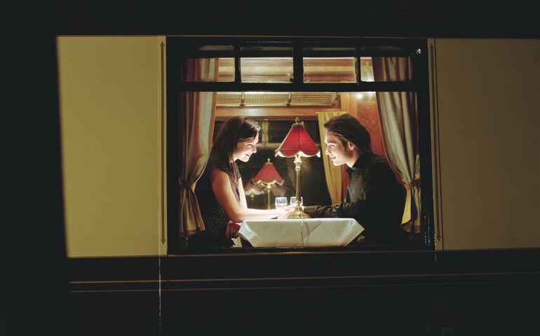 Young couple at table aboard train, exterior view, night