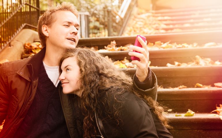 A young man interrupts his romantic endeavours to check something on his phone. His girlfriend looks surprised by the situation.