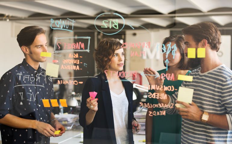 Business people discussing over plan on glass wall in office