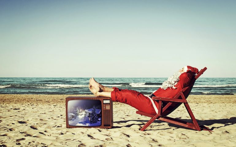Santa Claus on the beach, relaxing and sunbathing with feet resting on a vintage TV.