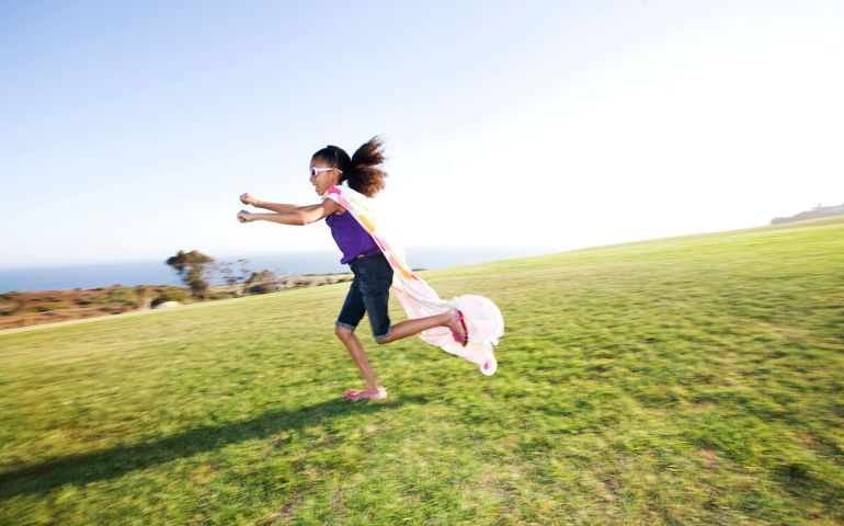 Little superhero running across a field