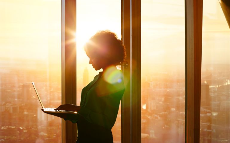 Businesswoman on laptop at window in morning sun