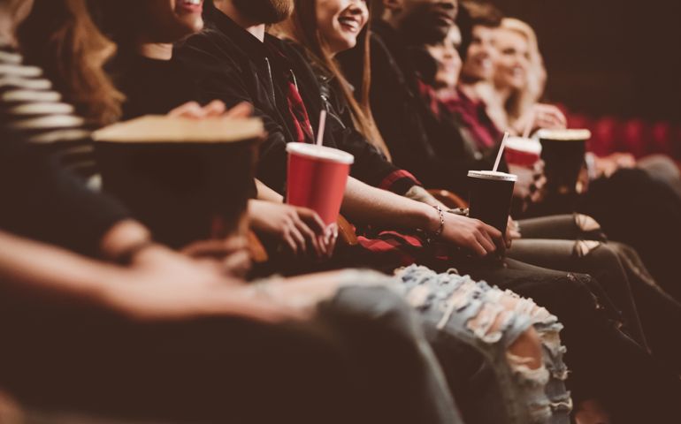 Group of people in the movie theater. Siede view, close up of hands, legs and drinks.
